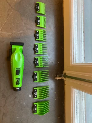 Grön hårtrimmer från TPOB med kammar - Elektrisk hårtrimmer från TPOB i grön plast med svart detalj. Medföljer åtta gröna kammar i olika storlekar för varierad längd på klippningen. Ergonomisk form och tydliga knappar gör den enkel att använda. Perfekt för hemmabruk eller salong.