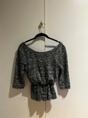 Gråmelerad topp med trekvartsärm - Snygg gråmelerad topp med trekvartsärm och bred urringning. Toppen har en markerad midja  som ger en cool och trendig look. Perfekt att matcha med både jeans och kjol.