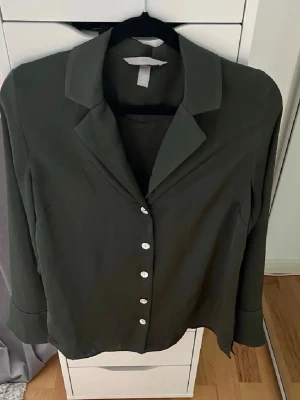 Mörkgrön blus med pärlemorknappar - Stilren mörkgrön blus med klassisk krage och pärlemorskimrande knappar framtill. 