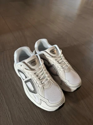 Dior b30 vit - Snygga vita Dior sneakers med detaljer i svart och grått. Skorna har en modern design med meshpaneler för extra andningsförmåga och läderdetaljer som ger en exklusiv känsla. Tjock sula i vitt och svart för en sportig look. Perfekta för dig som vill sticka ut.