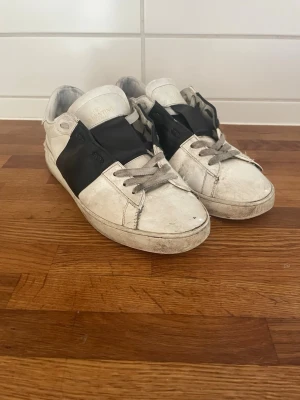 Valentino vita sneakers med svart detalj - Snygga vita sneakers från Valentino med en bred svart läderdetalj över sidan. Klassisk låg modell.  Perfekt för dig som gillar stilrena och exklusiva skor. Har ej låda till skorna.