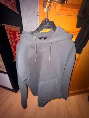 Mörkgrå hoodie från Next - Säljer en stilren mörkgrå hoodie från Next med klassisk känguruficka och justerbar dragsko i huvan. Hoodien har en avslappnad passform och är tillverkad i mjukt bomullsmaterial. Perfekt för dig som gillar en enkel och clean look.