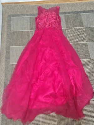 Lång röd balklänning med paljetter - Säljer en lång röd balklänning med transparent mesh upptill och detaljerad paljett- och broderad dekor på överdelen. Klänningen har en vid kjol i flera lager lagda i ett skirt material och är ärmlös för en elegant look.