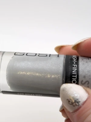 GOSH Stardust nagellack silvergrå 90% kvar - Nagellack från GOSH i nyansen 629 Milky Way. Färgen är silvergrå med skimrande glittereffekt och ger en shiny finish. Perfekt för dig som vill ha en stjärnstoft-look på naglarna. Kommer i en klassisk glasflaska med svart lock.