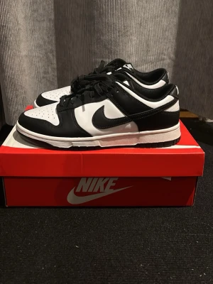 Nike Dunk Low Panda sneakers - Svarta och vita Nike Dunk Low sneakers med klassisk Swoosh-logga på sidan. Skorna har lågt ovalt snitt, svart-vit färgblockning och är tillverkade i läder med textildetaljer. Perfekta för dig som gillar stilrena och ikoniska sneakers.
