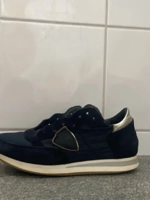 Philippe model GÄRNA BYTEN - Snygga mörkblå sneakers med silvriga detaljer vid hälen och på sidan. Ovandelen är i mocka och textil, med vit sula och låg profil. Lite mer använda än på första bilderna. Du kan se skicket på sista bilden. Storlek 36 och de är lite trånga på mig som har 38. Det går att tvätta så ser de helt nya ut. Tar gärna byten.