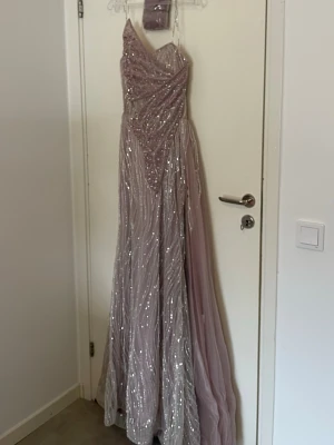 Ljuslila glittrig långklänning, butterfly  - En fantastisk ljuslila långklänning med glittriga paljettdetaljer och asymmetrisk axel. Klänningen har ett elegant fall och är perfekt till fest, förlovning mm. Helt ny, aldrig använt etiketten på, passar även 36