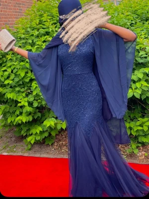 Marinblå långklänning med spets och paljetter - Elegant marinblå långklänning med figurnära passform, spetsdetaljer och glittriga paljetter. Klänningen har v-ringning, transparenta vida ärmar och volang nedtill. Perfekt för bal eller festliga tillfällen.