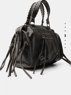 Svart handväska med fransar - Cool svart handväska med flätade handtag och långa fransdetaljer. Väskan har flera dragkedjefickor och silverfärgade metalldetaljer. Rymmer mycket! Använd fåtal gånger. Den större varianten. Från behrska 