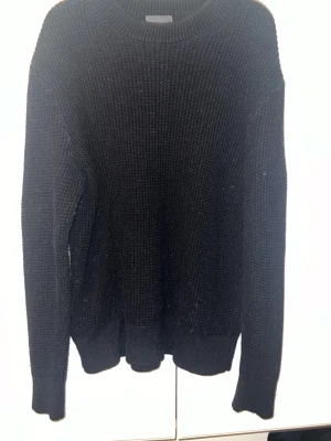 Svart stickad tröja från H&M - Klassisk svart stickad tröja från H&M i regular fit. Tröjan har rund halsringning, långa ärmar och ribbade muddar vid ärmslut och nederkant. Perfekt basplagg för lager på lager och enkel att matcha med allt.