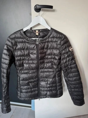 Svart dunjacka från Colmar - Snygg svart dunjacka från Colmar med quiltad design och rund halsringning. Jackan har dragkedja framtill och en diskret logotyp på ärmen. Perfekt för kalla vinterdagar och lätt att matcha med olika outfits.