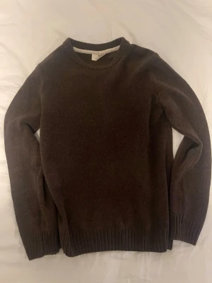 Mörkbrun stickad tröja - En enkel och stilren mörkbrun stickad tröja med rund halsringning och ribbade muddar vid ärmslut och nederkant. Perfekt för lager på lager och passar till det mesta i garderoben.