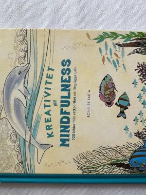 Oanvänd! Kreativitet och Mindfulness målarbok - En inspirerande bok med hård pärm i turkos och beige, fylld med hipsteraktiga undervattensillustrationer av delfiner och fiskar. Innehåller 100 bilder från vattenriket att färglägga själv, perfekt för dig som gillar kreativitet och mindfulness.