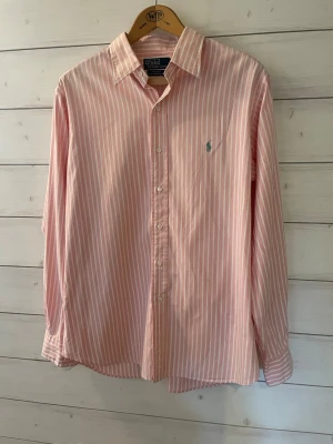 Ralph Lauren skjorta  - En snygg rosa Ralph Lauren skjorta med vita små ränder. Skjortan är i mycket fint skick!         Storlek 43(L-XL)                                                   Skriv gärna vid några frågor!