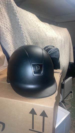 Svart ridhjälm från Samshield - Säljer en stilren svart ridhjälm från Samshield. Hjälmen har en matt finish och en diskret logga bak. Tillverkad i tåligt material med ventilation för extra komfort. Perfekt för dig som vill ha både säkerhet och snygg design i stallet.