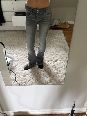 Grå bootcut jeans med hög midja - Säljer ett par grå bootcut jeans med hög midja och klassiska fem fickor. Jeansen har en snygg tvättad look och stängs med dragkedja och två knappar. Perfekta till en skön och fin outfit i sommar!☀️⛱️