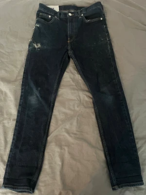 Mörkblå skinny jeans med slitningar - Snygga mörkblå skinny jeans med slitningar på vänster lår och klassiska fem fickor. Jeansen har en smal passform och kontrastsömmar. Perfekta för en trendig och avslappnad stil.