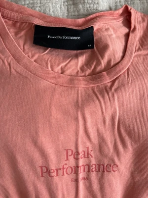 Rosa Peak Performance t-shirt - Snygg rosa t-shirt från Peak Performance med tryckt logga framtill. Klassisk rund halsringning och mjukt material som känns skönt mot huden. Perfekt för en avslappnad och sportig stil.