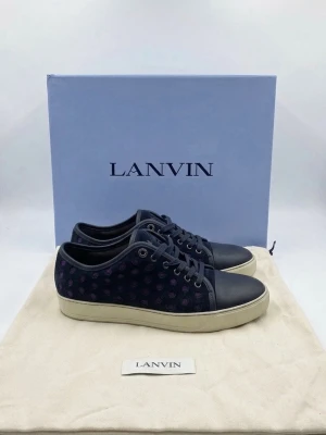 Mörkblå sneakers från Lanvin med box - Snygga mörkblå sneakers från Lanvin med box med lila prickar på sidan och vita sulor. Skorna har rund tå, svarta skosnören och detaljer i läder. Perfekta för dig som vill ha en unik och trendig look.