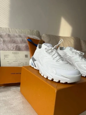 Louis Vuitton vita sneakers - Säljer ett par vita Louis Vuitton sneakers med chunky sula och diskreta LV-detaljer på sidan. Skorna har en modern design med inslag av grått och beige vid hälen. Tillverkade i en mix av läder och mesh för en exklusiv känsla. Perfekta för dig som gillar lyxiga streetwear-vibbar.