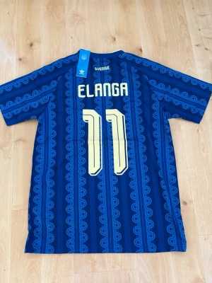 Elanga #11 – Sverige Borta (storlek M) - Elanga #11-tryck. Sverige Borta (blå). Storlek M. Helt ny och aldrig använd. Säljs i befintligt skick. Skickas snabbt! 🚚💨  Mått för denna tröja (storlek M): (Uppmätta av leverantör – viss variation kan förekomma) • Halva bröstmåttet: 53 cm • Tröjans längd: 74 cm • Ärmbredd: 23 cm • Axelbredd: 44 cm • Ärmlängd: 40 cm • Manschettbredd: 19 cm  🔥 Fan Edition – normal/mer avslappnad passform (något rymligare än Player Edition). 🇸🇪 Sverige landslag.