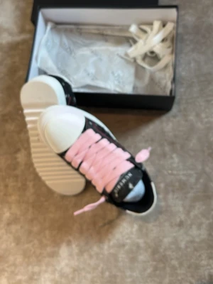 Numeris sneakers med rosa snören - Snygga sneakers från Numeris med svart ovandel dekorerad med vita prickar och rosa detaljer. Skorna har breda rosa skosnören och vit sula med räfflad kant. Tåhättan är vit och materialet ser ut att vara textil. Extra vita skosnören medföljer i lådan. Pris kan diskuteras vid snabb affär.