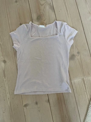 Ljusrosa topp från Gina Tricot - Säljer en ljusrosa topp från Gina Tricot med korta ärmar och en rak, enkel passform. Toppen har en mjuk och tunn känsla, perfekt för varmare dagar. Den har en diskret fyrkantig ringning och är lätt att matcha med olika stilar.