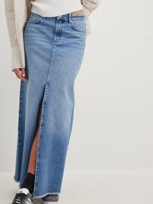 Lång jeanskjol med slits - Trendig lång jeanskjol i blå denim med låg midja och vidare/rak passform. Kjolen har en snygg slits framtill och rå kant nertill för en avslappnad look. Aldrig använd och lapparna kvar!