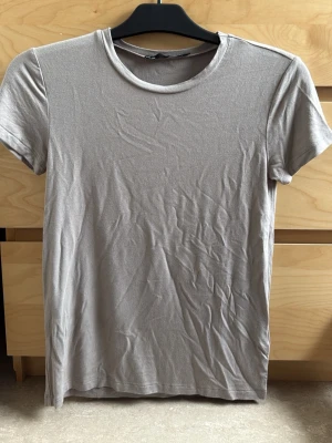 Beige basic t-shirt från 157 - En enkel och stilren beige t-shirt från 157 med rund halsringning och korta ärmar. Tillverkad i mjuk bomull som känns skön mot huden. Perfekt att matcha med jeans eller shorts för en clean look. (Aldrig använd) 