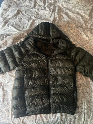 Mörkgrön peak performance dunjacka - Säljer en mörkgrön dunjacka med huva och dragkedja framtill. Jackan har två stora fickor med dragkedja och quiltad design. Perfekt för kalla vinterdagar och riktigt skön att bära. Materialet är glansigt och ger en modern look. Finns ett jätte litet hål på armen men syns knappast, pris kan förändras vid snabb affär 🤝