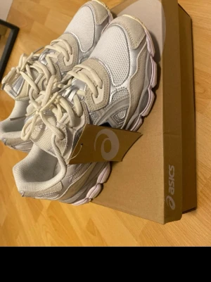 ASICS GEL - Snygga vita sneakers från ASICS med detaljer i mesh och mocka. Skorna har en chunky sula och klassisk snörning. Färgkombinationen är vit och beige med inslag av silver. Perfekta för dig som gillar sportig och trendig stil.