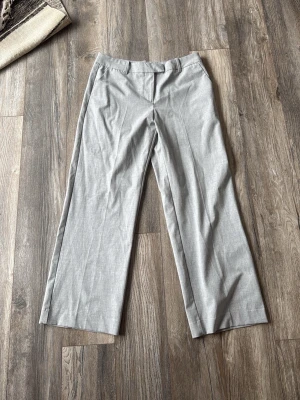 Ljusgrå vida kostymbyxor - Snygga ljusgrå kostymbyxor med raka, vida ben och klassisk passform. Byxorna har hällor för skärp, diskreta fickor fram och är tillverkade i ett tunt, vävt material som ger en stilren look. Använda en enstaka gång, byxorna är uppsydda och passar mig som är 165. Nypris 400