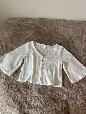 Vit blus från H&M - Säljer en söt vit blus med v-ringning och knappar framtill. Toppen har trekvartsärmar och är croppad i modellen. Väldigt skön och passar till mycket! Köpt på Sellpy i gott skick men själv aldrig använt💕