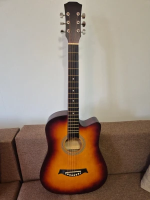 Solbrun akustisk gitarr - Säljer en akustisk gitarr med solbrun burst-finish och svart kant. Gitarren är stålstråndad med 6 strängar. Knappt använd i nyskick.. Perfekt för dig som vill börja spela eller bara jamma hemma. Denna gitarr i lindträ med en längd på cirka 96 cm är ett utmärkt val för yngre musikanter eller vuxna nybörjare som söker ett lättspelat instrument. Den något mindre storleken gör gitarren lättare att hålla och spela på, särskilt för barn eller personer med mindre händer.