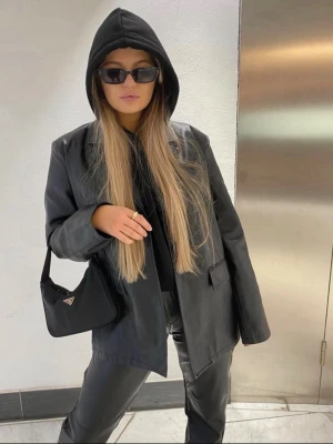Svart oversized skinnjacka - Snygg svart skinnjacka i oversized modell med breda slag och två stora fickor framtill. Jackan har en rak passform och stängs med knappar. Fått av min syster så vet ej vart den är ifrån . Men är i bra sick använd fåtal gånger , passar både 36 och 38 skulle jag säga 