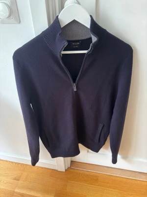 Mörkblå zip Massimo Dutti - Mörkblå stickad tröja från Massimo Dutti med halv dragkedja och hög ribbad krage i kontrasterande grått. Tröjan har långa ärmar och två diskreta fickor framtill. Perfekt för lager på lager och stilrena outfits.
