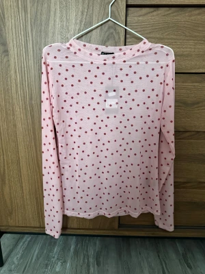 Rosa mesh topp med röda prickar - Säljer en tunn och transparent rosa mesh topp från Monki med röda prickar över hela. Toppen har lång ärm och en högre rundad hals. Perfekt att styla lager på lager för en trendig look.