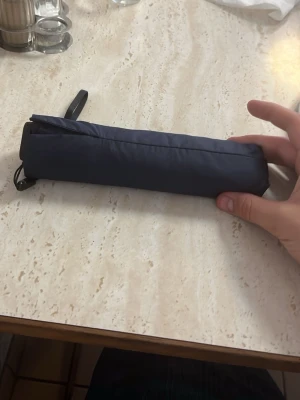 Mörkblå hopfällbar paraply - Snyggt och smidigt mörkblått hopfällbart paraply med handrem. Perfekt att ha i väskan när vädret är oförutsägbart. Paraplyet har en enkel och stilren design utan synligt märke.