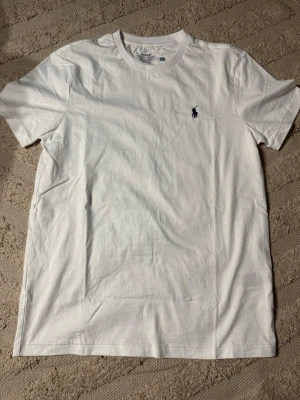 Vit t-shirt från Polo Ralph Lauren - Klassisk vit t-shirt från Polo Ralph Lauren med rund halsringning och broderad marinblå logga på bröstet. Modellen är slim fit och tillverkad i mjuk bomull. Kom om vid frågor!