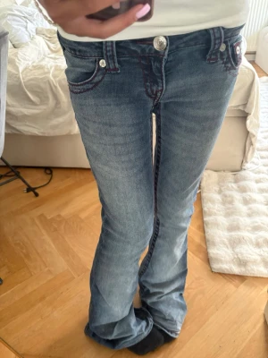 True Religion bootcut jeans blå - KAN SÄNKA PRISET!! Säljer ett par blå bootcut jeans från True Religion med röda kontrastsömmar och ikoniska bakfickor. Jeansen har låg midja, de är lite långa för mig som är 153