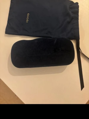 Svarta solglasögon från Gucci - Snygga svarta solglasögon från Gucci med fyrkantiga glas och tunna metallbågar. Kommer med originalfodral, putsduk och tygpåse med Gucci-logga. Perfekta för dig som vill ha en stilren och exklusiv accessoar.
