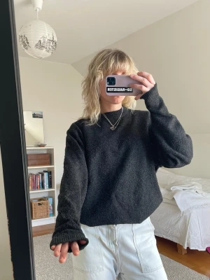 Svart stickad tröja med rund hals - En enkel och stilren svart stickad tröja med rund hals och långa ärmar. Tröjan har en något lös passform och ribbstickade muddar vid ärmslut och nederkant. Perfekt att matcha med jeans eller kjol för en avslappnad look.