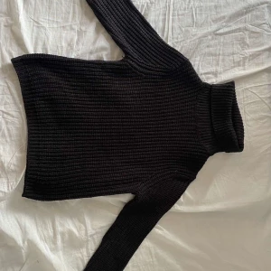 Svart stickad polotröja Rut&Circle - Mysig svart stickad polotröja från Rut&Circle i storlek S. Tröjan har en hög, ribbad polokrage och grovstickad struktur. Perfekt för lager-på-lager och passar till både jeans och kjol. Långärmad och klassisk modell som är enkel att styla.