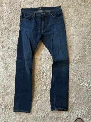 Mörkblå jeans från Lee - Snygga mörkblå jeans från Lee med klassisk femficksdesign och raka ben. Jeansen har en diskret Lee-logga på bakfickan och är gjorda i slitstarkt denim-material. Perfekt för dig som gillar en tidlös och enkel look.