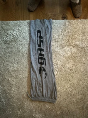 Gråa gym-byxor från GASP - Mysiga gråa loungewear-byxor från GASP med svart tryck längs ena benet. Byxorna har resår i midjan och vid bensluten för en avslappnad passform. Perfekta för chill hemma eller till gymmet. Tillverkade i mjukt och tunt material.