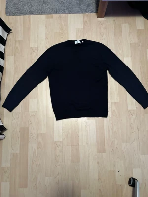Svart tröja från BÄCK - En enkel och stilren svart stickad tröja med rund hals och långa ärmar. Perfekt för att matcha med jeans eller chinos. Tröjan har en klassisk passform och ribbade muddar vid ärmslut och nederkant. Tröjan har använts väldigt lite. Köpt för cirka ett år sen och har legat i garderoben länge. Hör av er vid frågor eller funderingar👍✅