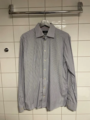 Randig skjorta från Eton - Klassisk skjorta från Eton med tunna blå och vita ränder. Skjortan har lång ärm, knappar framtill och på manschetterna samt en stilren krage. Tillverkad i ett tunt och skönt bomullstyg som passar perfekt till en dressad look.