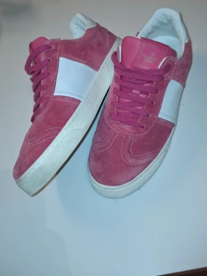 Rosa sneakers från Valentino - Snygga rosa sneakers från Valentino i mocka med vita detaljer och bred vit rand på sidan. Skorna har rosa snörning, vit sula och coolt kamouflagemönster undertill. Insidan är vit och märket syns på plösen och innersulan.Storleken är 39/5 men passar 40, kanske 41.