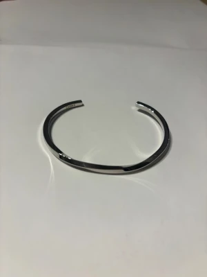 Silvrigt minimalistiskt armband - Snyggt och stilrent armband i silverfärgad metall med öppen design. Armbandet har en slät, blank yta och en enkel, modern form som passar perfekt till en clean look.  Säljer då jag inte passar i silver.
