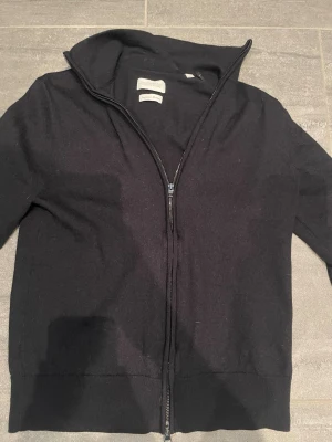 Svart ziptröja från These glory of the days - Klassisk svart ziptröja från These glory of the days med hög krage och hel dragkedja framtill. Tröjan har ribbade muddar vid ärmslut och nederkant, och är tillverkad i mjukt material, den är slim fit k sitter riktigt bra på. Den har inga defekter. Kom med frågor o prisförslag om ni har